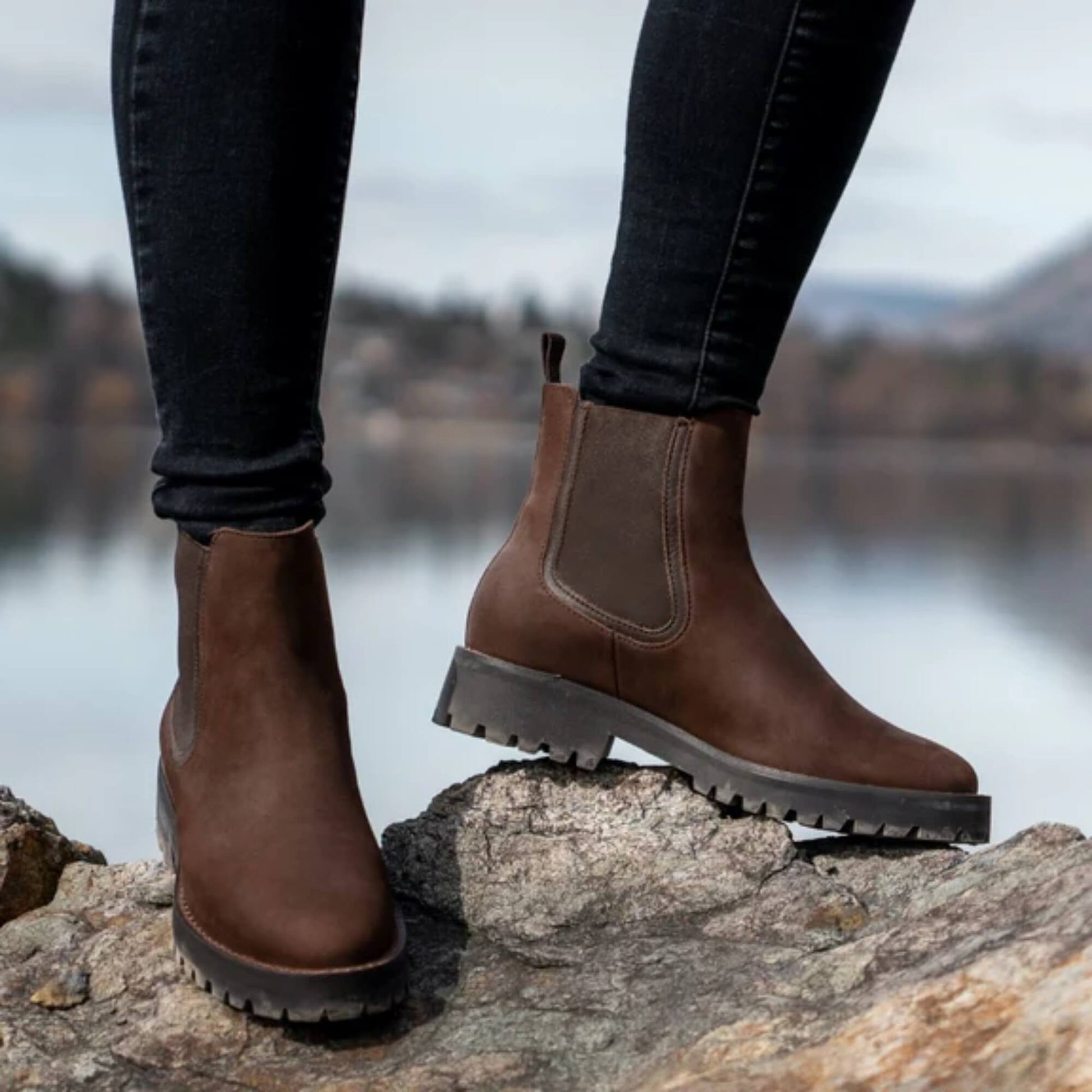 Mujer de pie junto al lago usando botines Kalver Sierra café en otoño