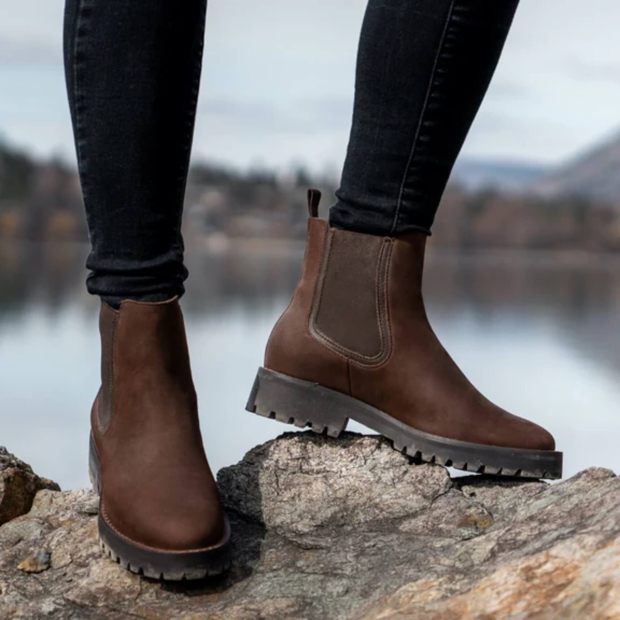 Mujer de pie junto al lago usando botines Kalver Sierra café en otoño