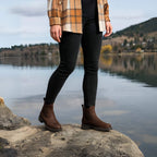 Mujer usando botines cuero Kalver Sierra café sobre roca con paisaje invernal